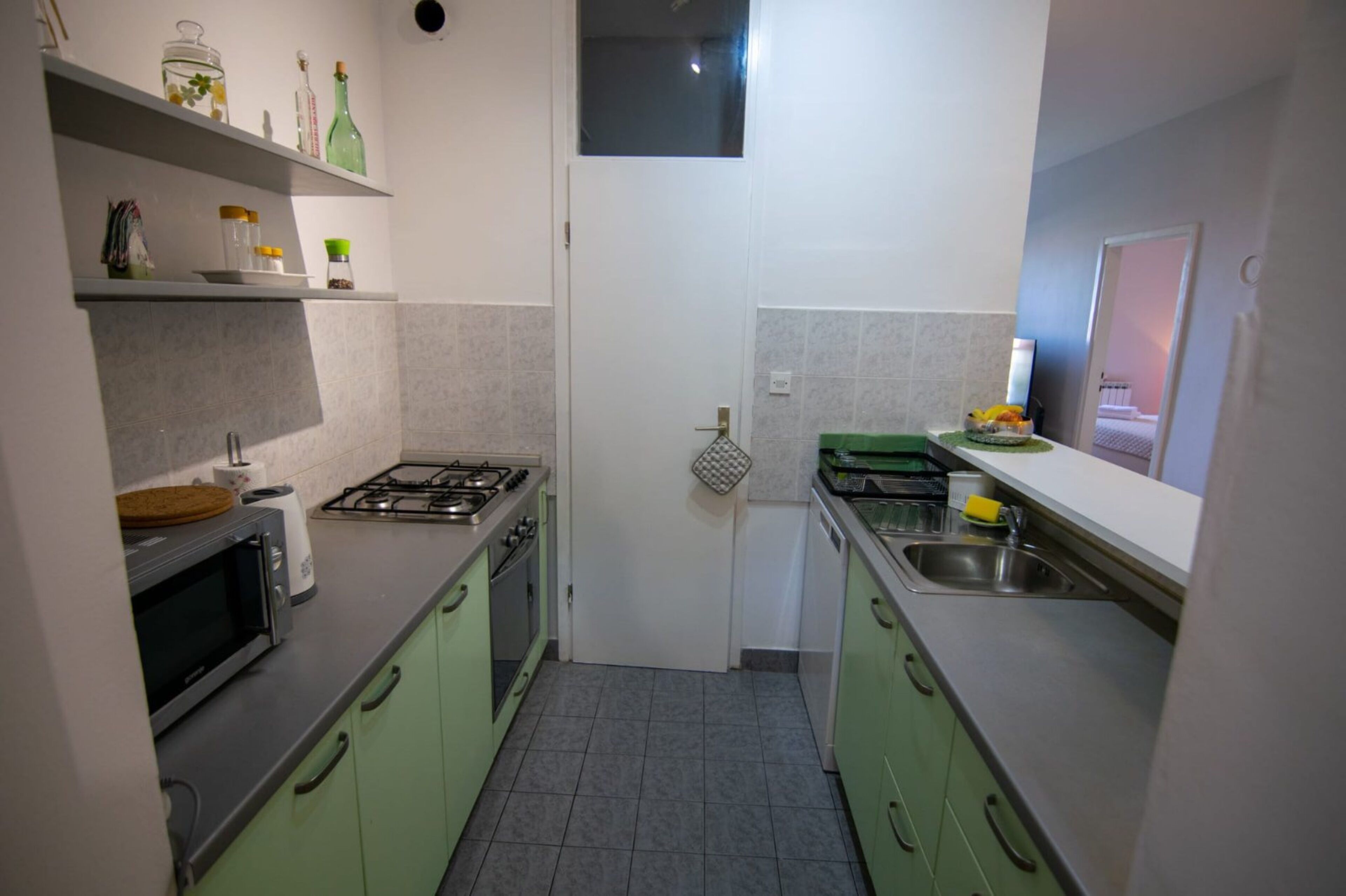 A compact kitchen with green cabinets, a gas stove, a microwave, and a sink.