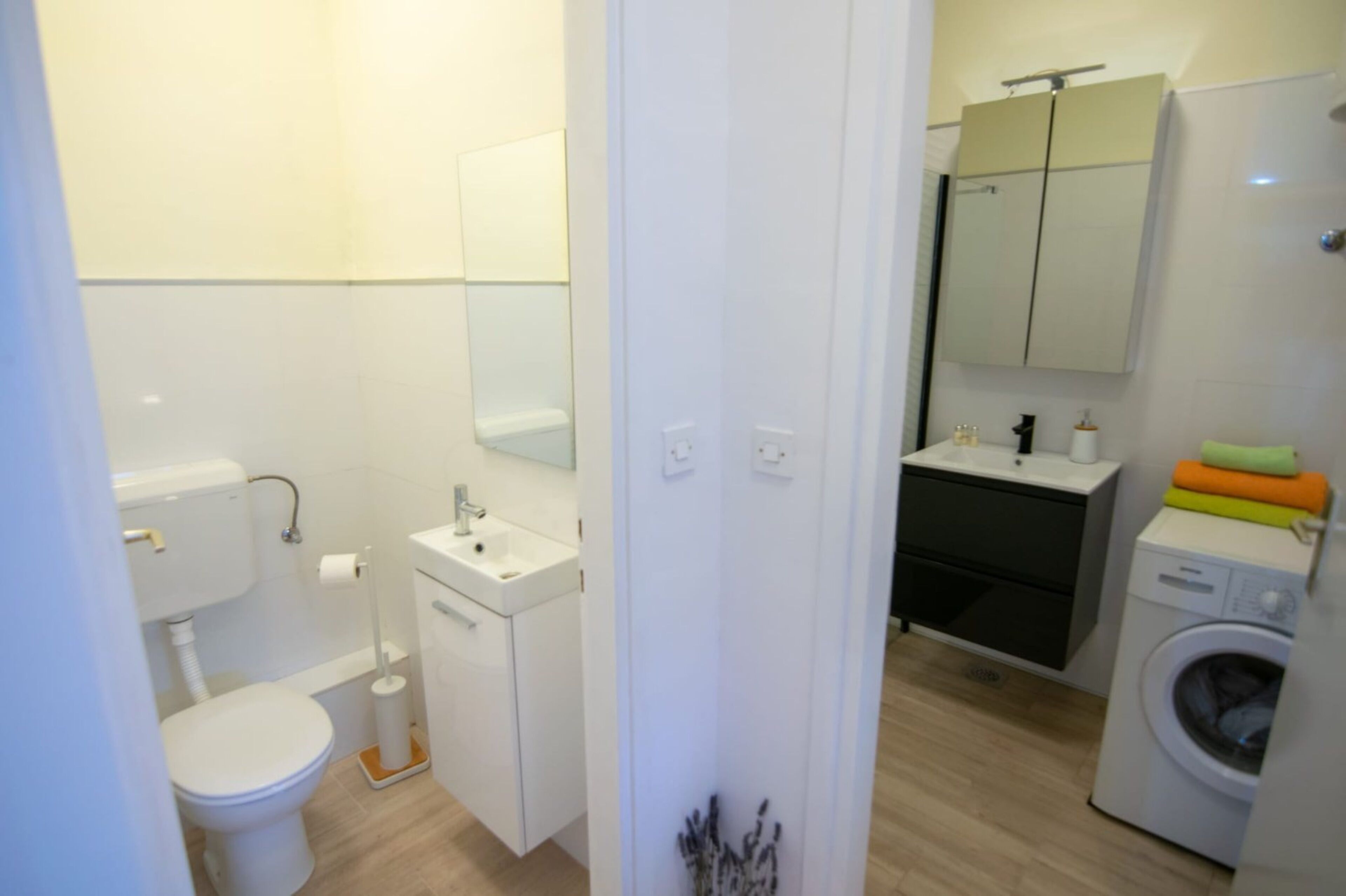 Ein modernes Badezimmer mit Toilette, Waschbecken, Spiegel und Waschmaschine.