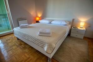 Ein ordentlich bezogenes Bett mit einer gesteppten Decke, zwei Nachttischlampen, einem Heizkörper und einem Holzboden.