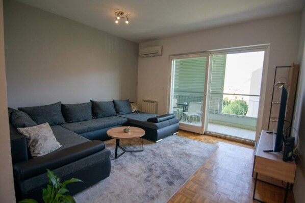 Ein modernes Wohnzimmer mit einer Eckcouch, einem Couchtisch und einer Schiebetür zu einem Balkon.