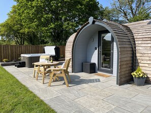 A cozy outdoor patio with a wooden table and chairs, a hot tub, and a covered seating area. - Y Dderwen (Ruthin)