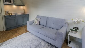 Ett kompakt bostadsutrymme med ett litet pentry, en grå soffa och ett litet vitt bord med en krukväxt.