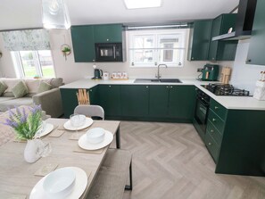 Une cuisine moderne avec des meubles de couleur verte, un four à micro-ondes encastré et une cuisinière à gaz.
