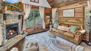 A cozy cabin interior with a stone fireplace, a wooden ceiling, and a large window with curtains. - CastAway Waterfront Rustic Cabin Very Private With Outdoor Cabana (Waynesville)