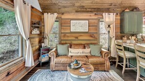 A cozy cabin interior with a leather sofa, a round coffee table, and a rustic wooden ceiling. - CastAway Waterfront Rustic Cabin Very Private With Outdoor Cabana (Waynesville)