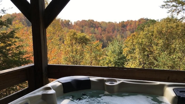 A hot tub with a wooden deck and a view of autumn foliage. - Secluded, Great View! Hot Tub, Wood Fireplace, Screened in Porch, Arcade Games. (Rogers)