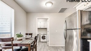 A compact kitchen with a stainless steel refrigerator, a built-in washer-dryer, and a dining area with a wooden table and chairs.
