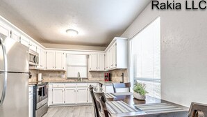 A modern kitchen with white cabinets, stainless steel appliances, and a dining area with a striped tablecloth and chairs.