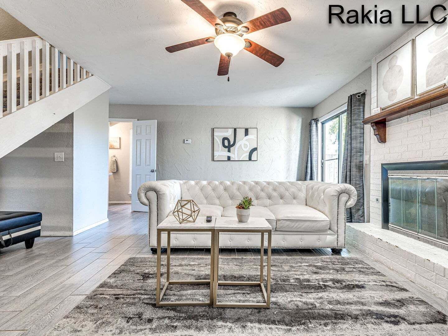 Un salon avec un canapé blanc, une table basse, un ventilateur de plafond, une cheminée et un escalier.