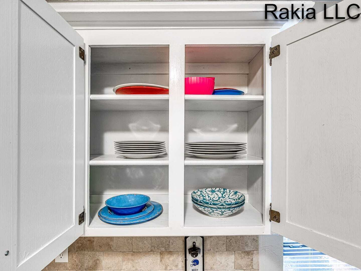 Ein weißes Schrank mit Regalen, auf denen Teller, Schüsseln und eine rote und blaue Schale stehen.