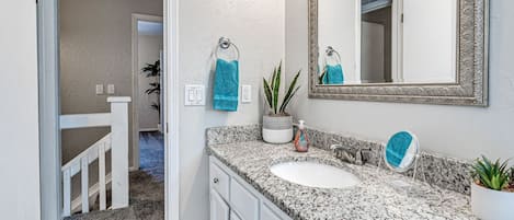 Un baño con encimera de granito, dos lavamanos, un espejo grande y una planta en maceta.