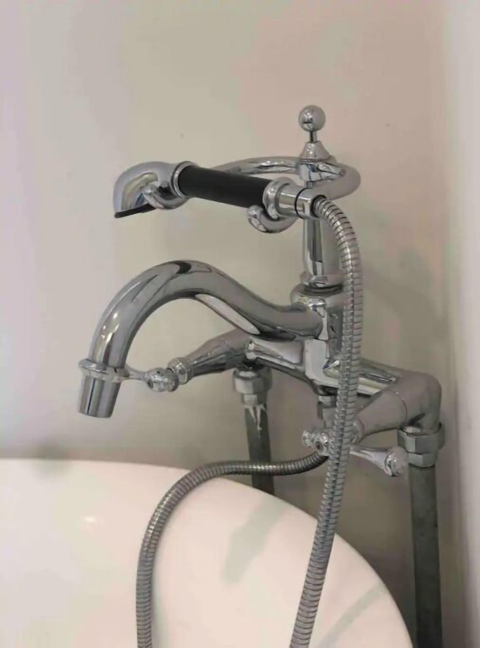 A bathroom with a chrome faucet, a handheld showerhead, and a visible water pipe.