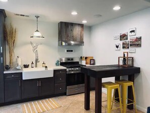 A modern kitchen with dark cabinetry, stainless steel appliances, a central island with stools, and wall-mounted artwork.