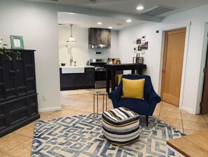 A modern living room with a dark blue armchair, a patterned rug, and a striped ottoman.