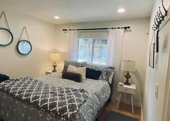 A bedroom with a bed, two bedside tables, a window with curtains, and wall-mounted decor.