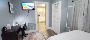 A bedroom with a bed, a desk with a chair, a television mounted on the wall, and a door leading to a bathroom. - Clean/Cozy Studio 2-Near DT Indianapolis/Queen Bed (Indianapolis)
