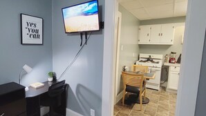 Habitación con escritorio, silla, planta pequeña en maceta, televisor montado en la pared y una cita inspiradora enmarcada.