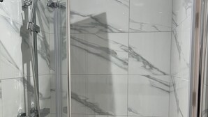 A modern shower enclosure with a glass door, chrome fixtures, and marble-patterned tiles. - Entire Studio apartment - London  (London)
