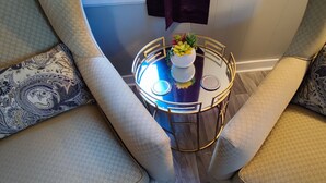 Una habitación moderna con una mesa redonda de vidrio, dos sillones estampados y una pequeña planta decorativa.