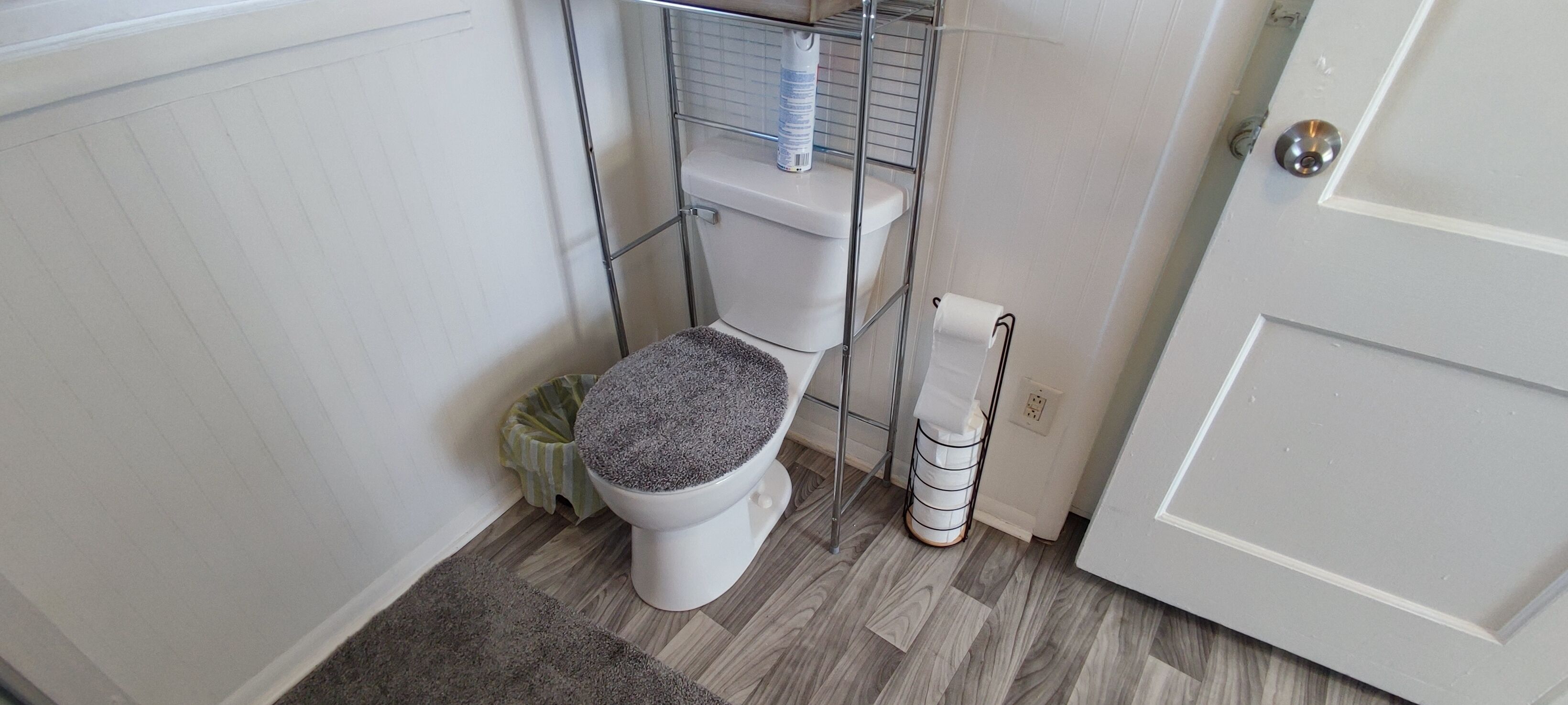 A small bathroom with a toilet, a metal shelf above the toilet, a toilet paper holder, and a door.