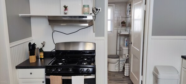 A compact kitchen with a stove, white cabinets, and a small window.