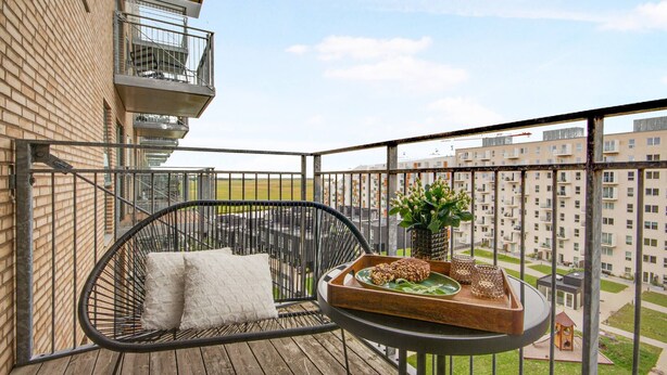 A balcony with a wicker chair, a small table with a tray of food, and a view of surrounding buildings. - Modern Apartment Close to Royal Arena (Kastrup)