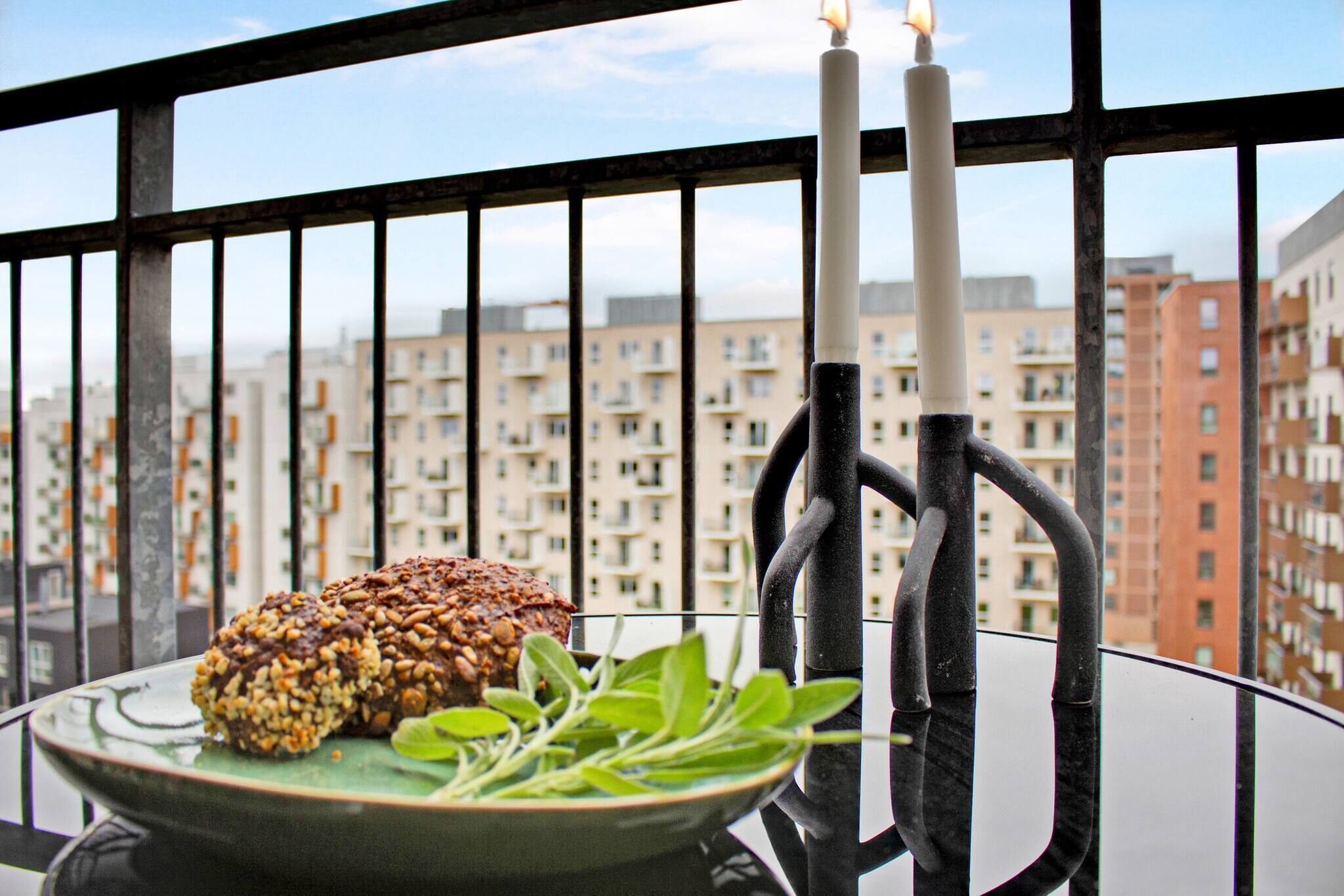A balcony with a plate of food, two candles, and a view of apartment buildings.