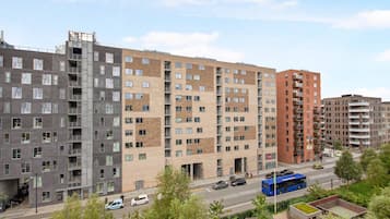 A multi-story residential building with a mix of brick and concrete facades, balconies, and a blue bus on the street.