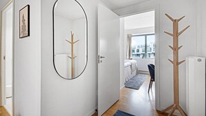 A hallway with a coat rack, a mirror, and a framed picture on the wall. - Modern Apartment Close to Royal Arena (Kastrup)