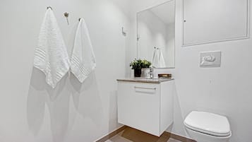 A modern bathroom with white fixtures, a toilet, a sink with a mirror, and two towels hanging on the wall.