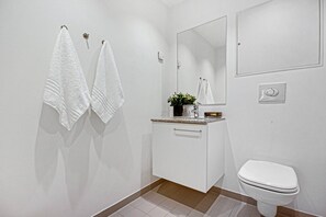 A modern bathroom with white fixtures, a toilet, a sink with a mirror, and two towels hanging on the wall.