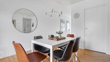 A dining area with a white table, black and brown chairs, a chandelier, and a round mirror on the wall.