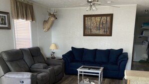 A living room with a dark blue sofa, a grey recliner, a glass coffee table, and a ceiling fan.