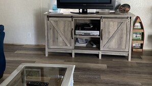 A living room with a television on a wooden cabinet, a glass coffee table, and framed pictures on the wall.