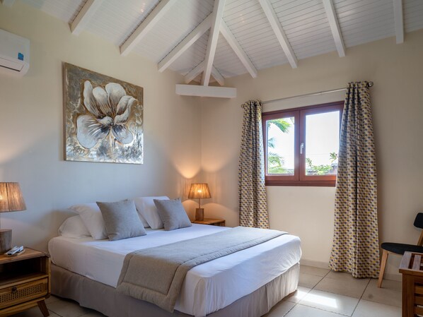 A bedroom with a bed, two bedside lamps, a window with curtains, a ceiling fan, and a wall-mounted air conditioner.