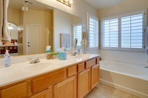 A bathroom with a large mirror, two sinks, wooden cabinets, a bathtub, and a window with blinds. - 1 Mi to Surprise Stadium! Home w/ Patio & Hot Tub (Surprise)
