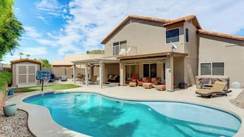 Une maison avec une piscine, du mobilier de jardin et un espace extérieur aménagé avec un coin salon couvert.