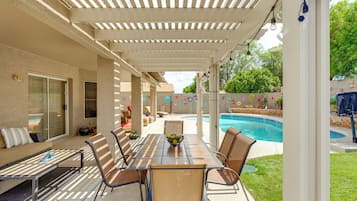 Une terrasse extérieure avec une table et des chaises, une piscine et un espace abrité agrémenté d’une pergola.