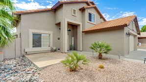 A two-story house with a tiled roof, a front porch with a bench, and a small garden with palm trees and a cactus. - 1 Mi to Surprise Stadium! Home w/ Patio & Hot Tub (Surprise)