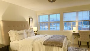 Een slaapkamer met een groot bed, een nachtkastje, een stoel en een raam met zonwering.