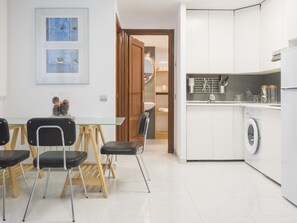 Een moderne keuken met een ingebouwde wasmachine, een eethoek met een glazen tafel en stoelen, en een gang die leidt naar een badkamer.