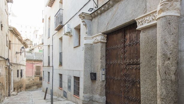 Une ruelle pavée étroite bordée de bâtiments historiques, une grande porte en bois et une enseigne en métal.