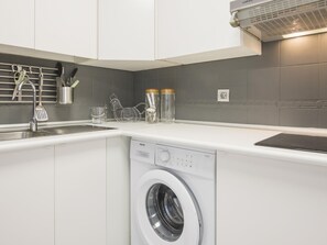 Een compacte keuken met een inbouw wasmachine, een spoelbak en een keukengerei houder.