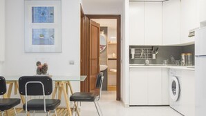 Une cuisine moderne avec des meubles blancs, un lave-linge et un coin repas comprenant une table en verre et des chaises noires.