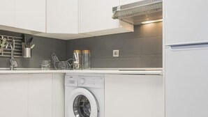 Une cuisine moderne avec des armoires blanches, un lave-linge encastré et une hotte de cuisine en acier inoxydable.