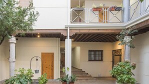 Une cour spacieuse avec une porte en bois, des plantes en pot et un escalier menant à un balcon.