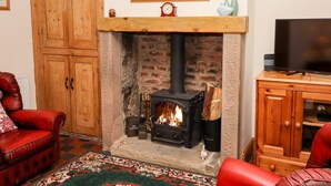 A cozy living room with a fireplace, wooden furniture, and a television. - Longstone View (Bakewell)