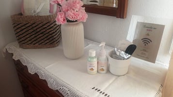 A bathroom vanity with a white lace doily, a woven basket, a vase with pink flowers, and toiletries.