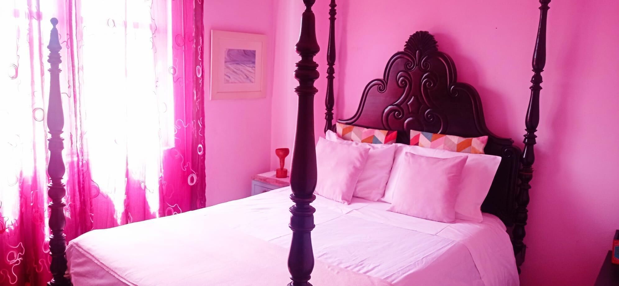 A bed with a wooden headboard, white bedding, and pink curtains.