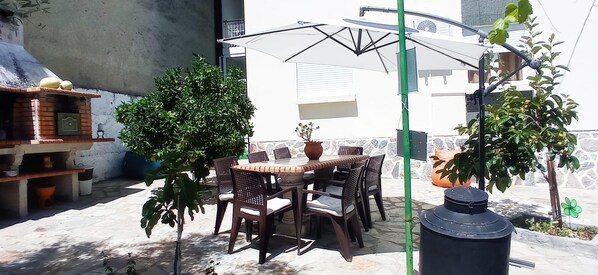 An outdoor patio with a table and chairs, surrounded by potted plants and a barbecue grill.
